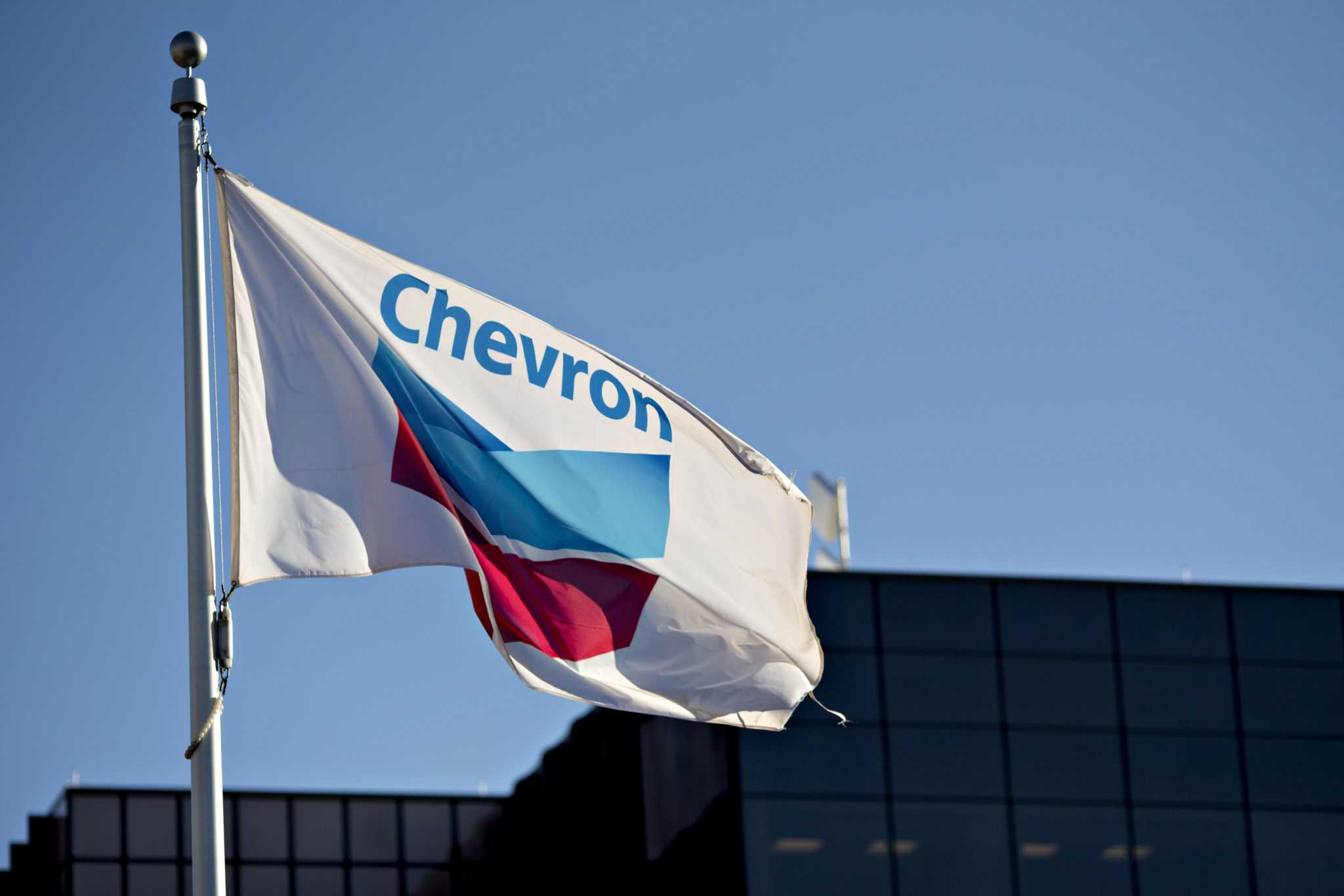 A Chevron Corp. flag flies outside an office building in Midland, Texas, U.S., on Thursday, March 1, 2018. Chevron, the world's third-largest publicly traded oil producer, is spending $3.3 billion this year in the Permian and an additional $1 billion in other shale basins. Its expansion will further bolster U.S. oil output, which already exceeds 10 million barrels a day, surpassing the record set in 1970. Photographer: Daniel Acker/Bloomberg
